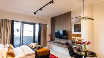 A modern hotel room with a bed, a dining area, and a TV.