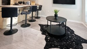 A modern kitchen with a built-in oven, a dining area with a round table and chairs, and a large TV mounted on the wall displaying 'NETFLIX'. - The Luxe Black Haven (340) (Des Moines)