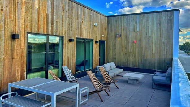 Un patio exterior con paneles de madera, puertas de cristal y zonas de estar.
