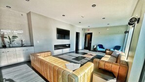 Una sala de estar moderna con un sofá seccional, un televisor de pantalla plana montado en la pared y una zona de comedor con mesa y sillas.