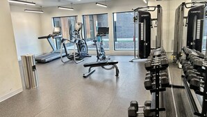 Un gimnasio con cintas de correr, elípticas, una banca y un estante con mancuernas.
