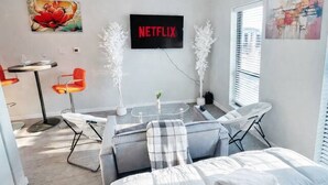 A modern hotel room with a bed, a desk, and a chair. There is a wall-mounted TV displaying 'NETFLIX' and artwork on the walls. - Zesty Orange Abode (438) (Des Moines)