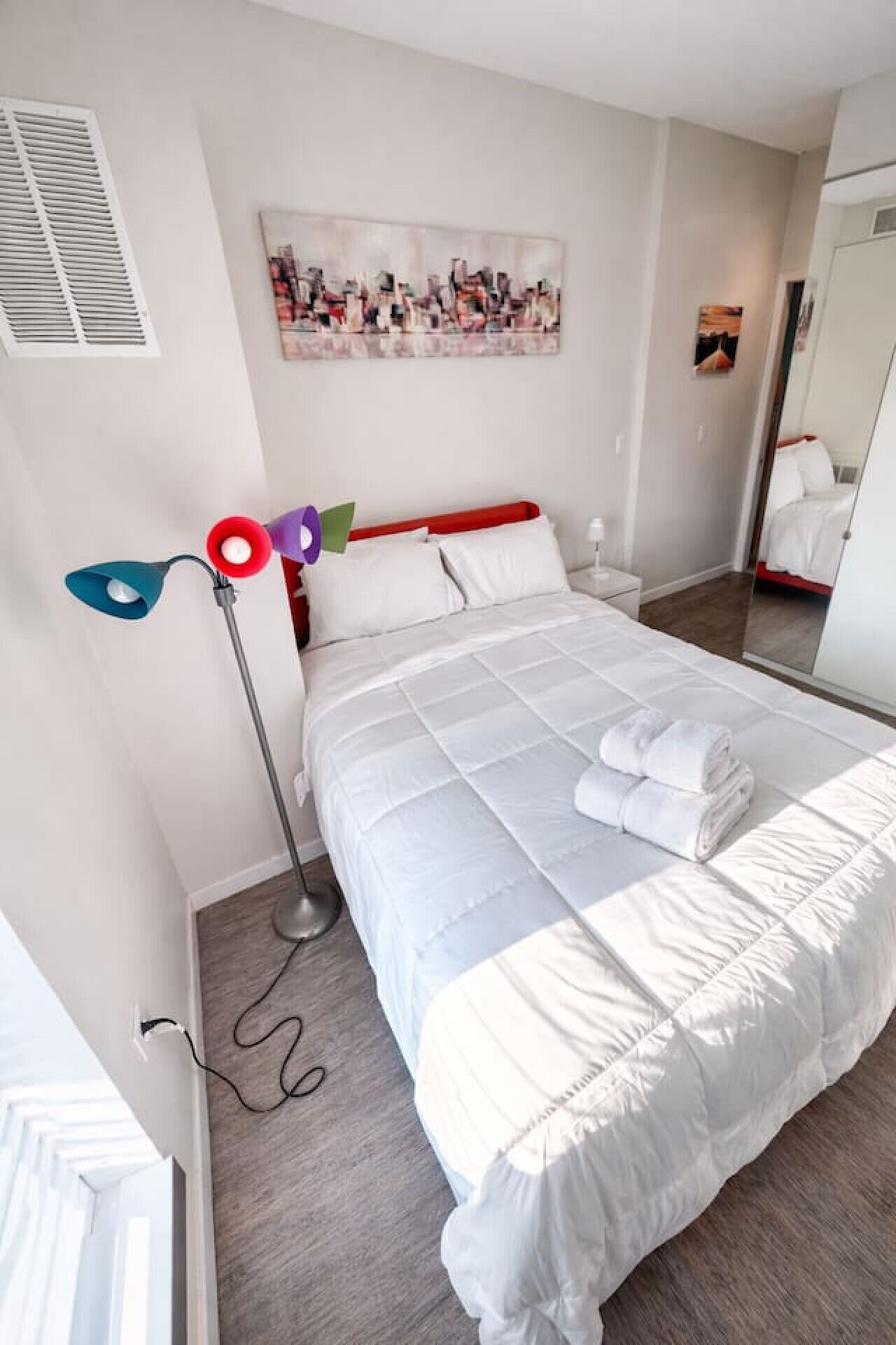 Een hotelkamer met een bed, nachtkastje, lamp en schilderij aan de muur.