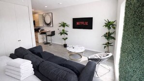 Una sala de estar moderna con un sofá, una mesa de centro y un televisor que muestra 'NETFLIX'.