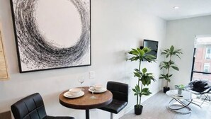 Un comedor moderno con una mesa redonda, dos sillas negras y un cuadro abstracto grande en la pared.