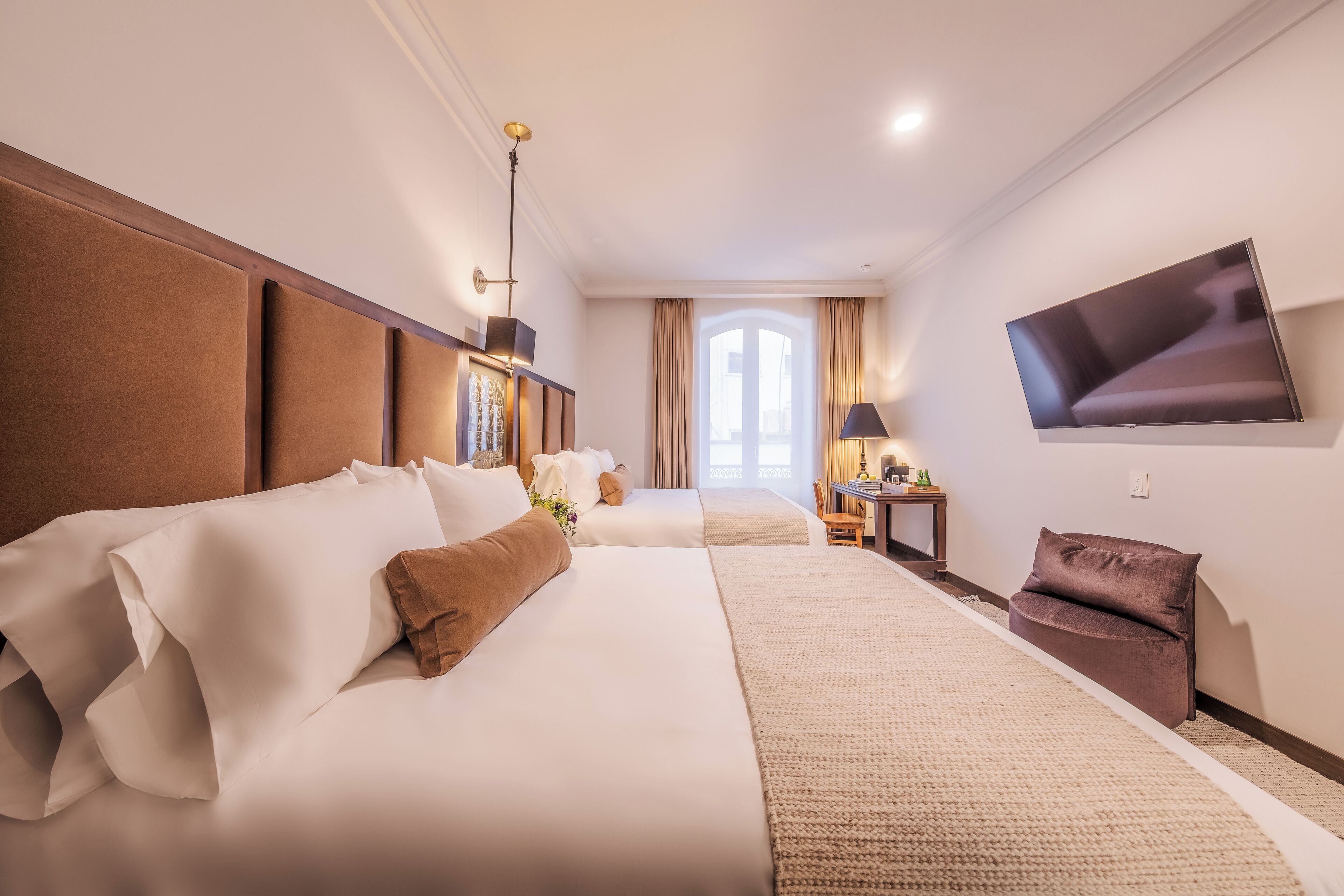 A hotel room with a large bed, a flat-screen TV mounted on the wall, and a window with curtains.