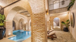 An indoor swimming pool with brick arches, a lounge area with a massage chair, and a staircase leading to an upper level. - Casa Kloster Hotel Boutique (Guanajuato)