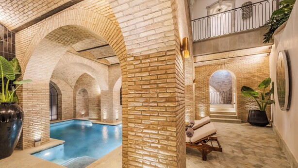 An indoor swimming pool with brick arches, a lounge area with a massage chair, and a staircase leading to an upper level. - Casa Kloster Hotel Boutique (Guanajuato)
