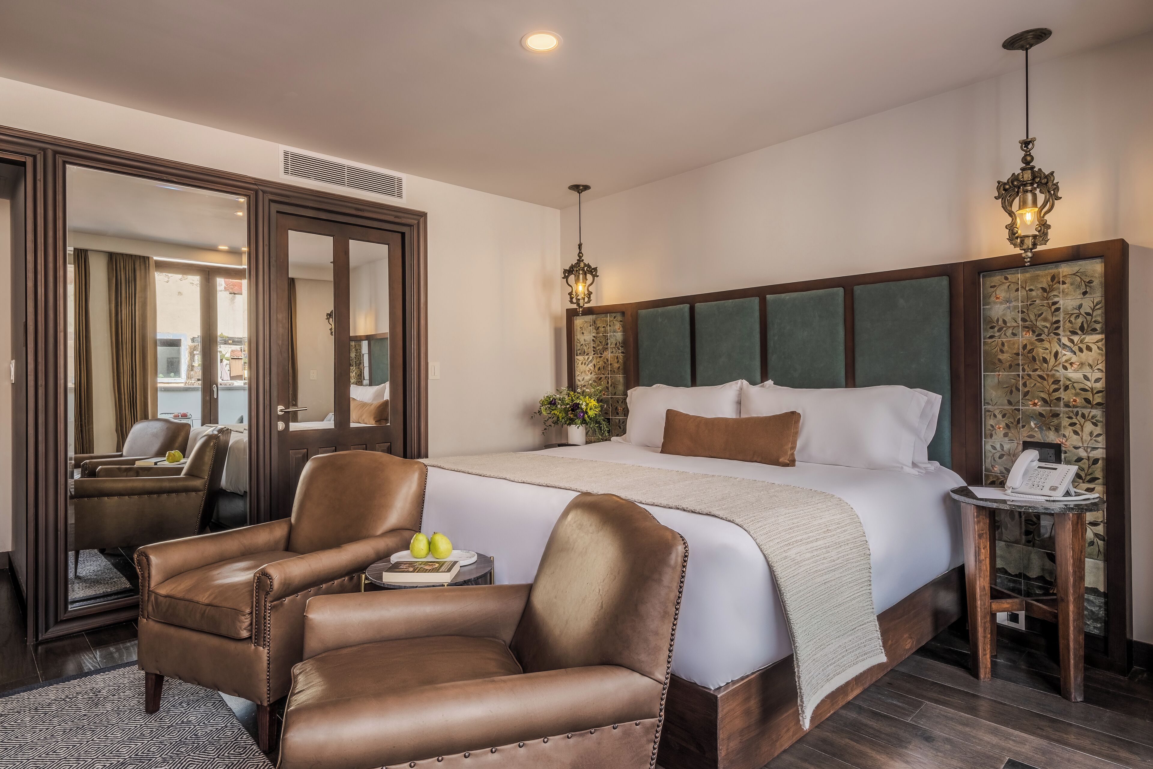 A hotel room with a large bed, two leather chairs, a bedside table with a phone, and a mirror.