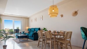 Un saló modern amb un sofà color turquesa, una taula de menjador amb cadires de vimetla i un finestral gran que ofereix una vista.