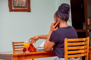 Une personne est assise à une table en bois, devant un verre de jus d’orange et une assiette de nourriture, et est en train de téléphoner.