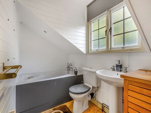 Une salle de bain équipée d’une baignoire, de toilettes et d’un lavabo, avec un plafond en pente et une fenêtre.