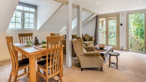 A dining area with a wooden table and chairs, a sofa, and a small stool. There is a window with a view of greenery outside. - Casa BowWow - UK48047 (Rudry, near Cardiff)
