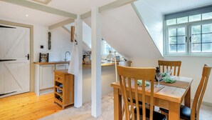 A dining area with a wooden table and chairs, a kitchen in the background, and a window with a view of trees. - Casa BowWow - UK48047 (Rudry, near Cardiff)