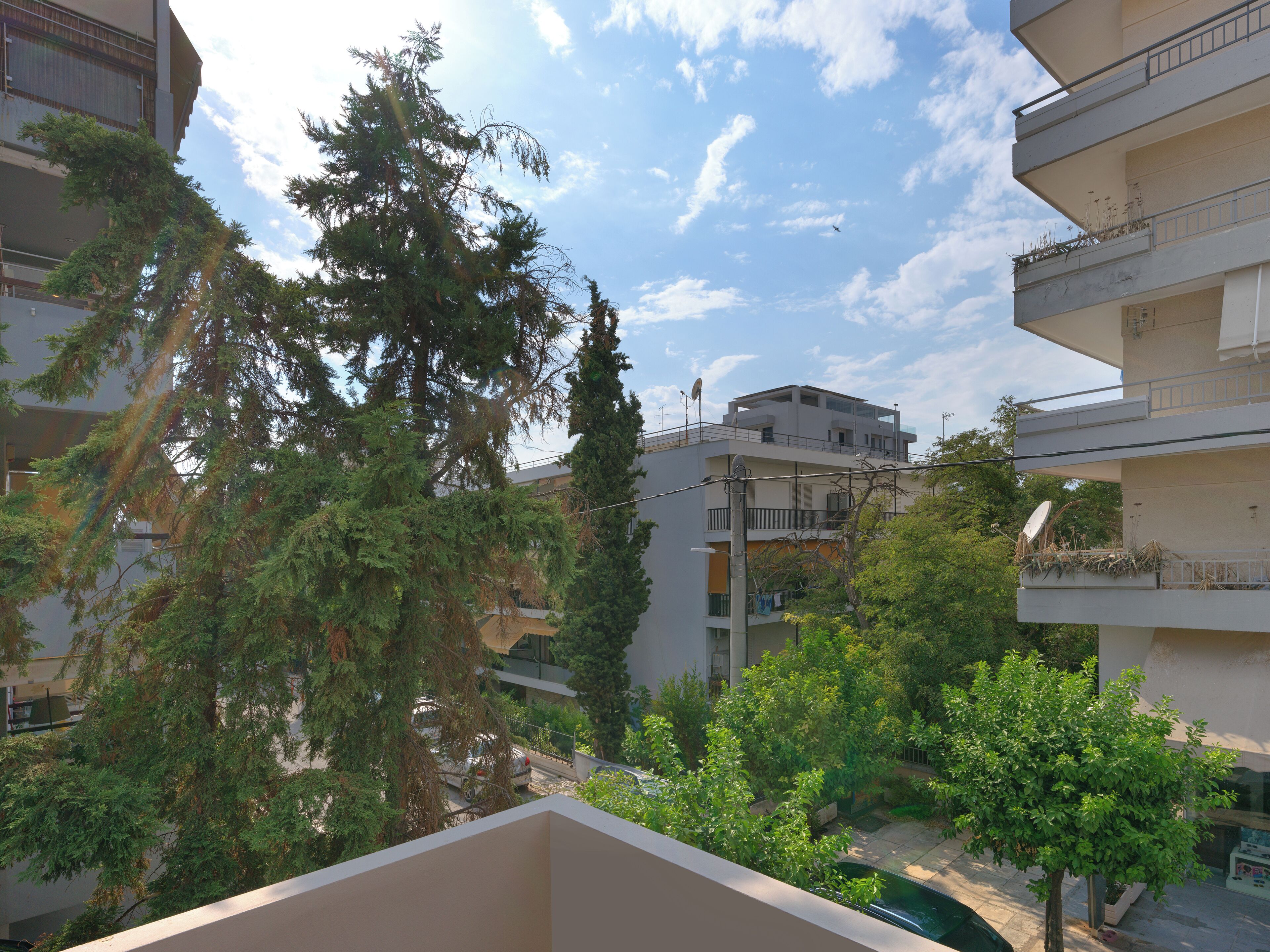 A residential building with multiple balconies, a clear sky, and surrounding greenery.