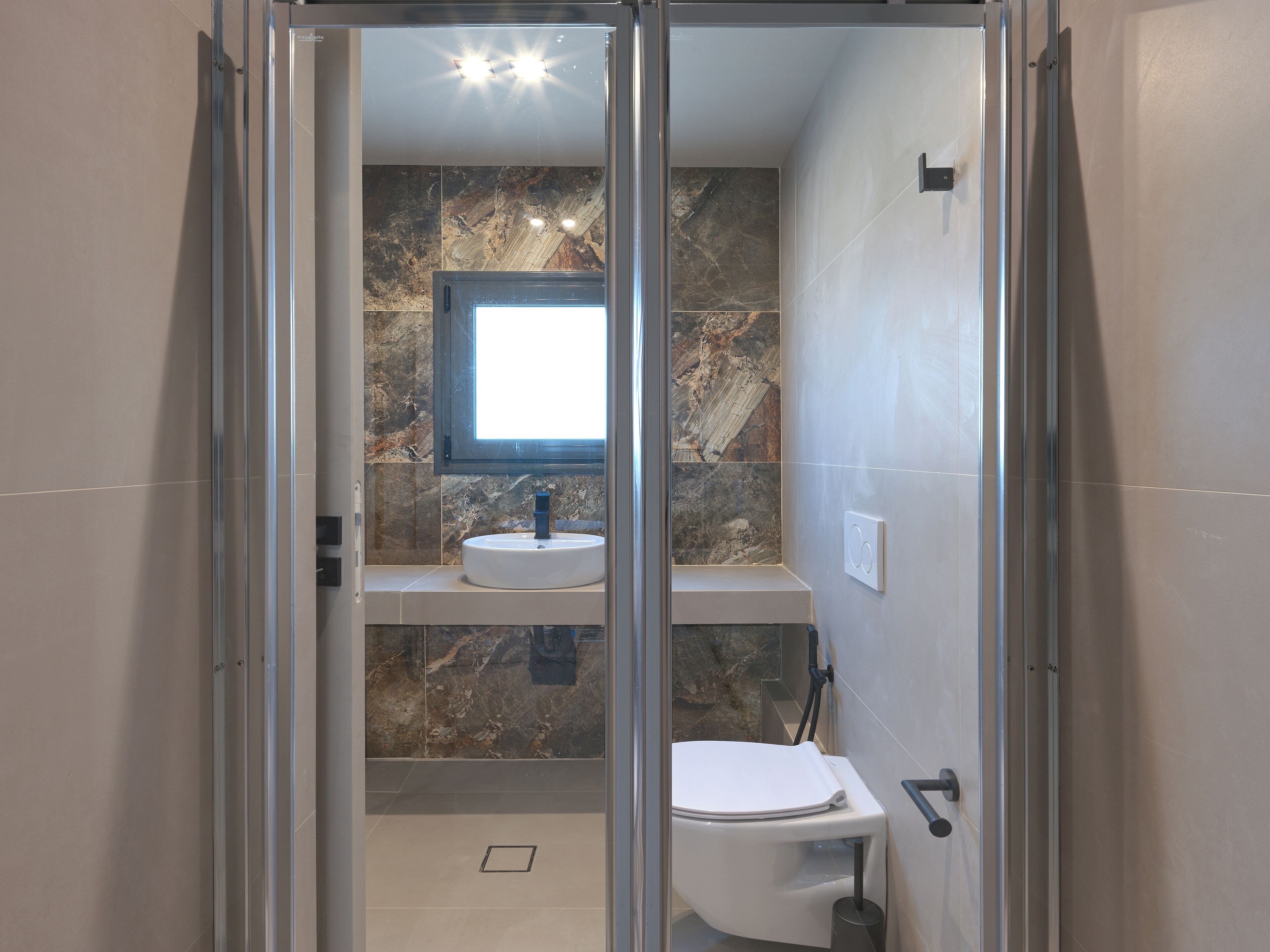 A modern bathroom with a glass shower enclosure, a marble backsplash, and a white sink.