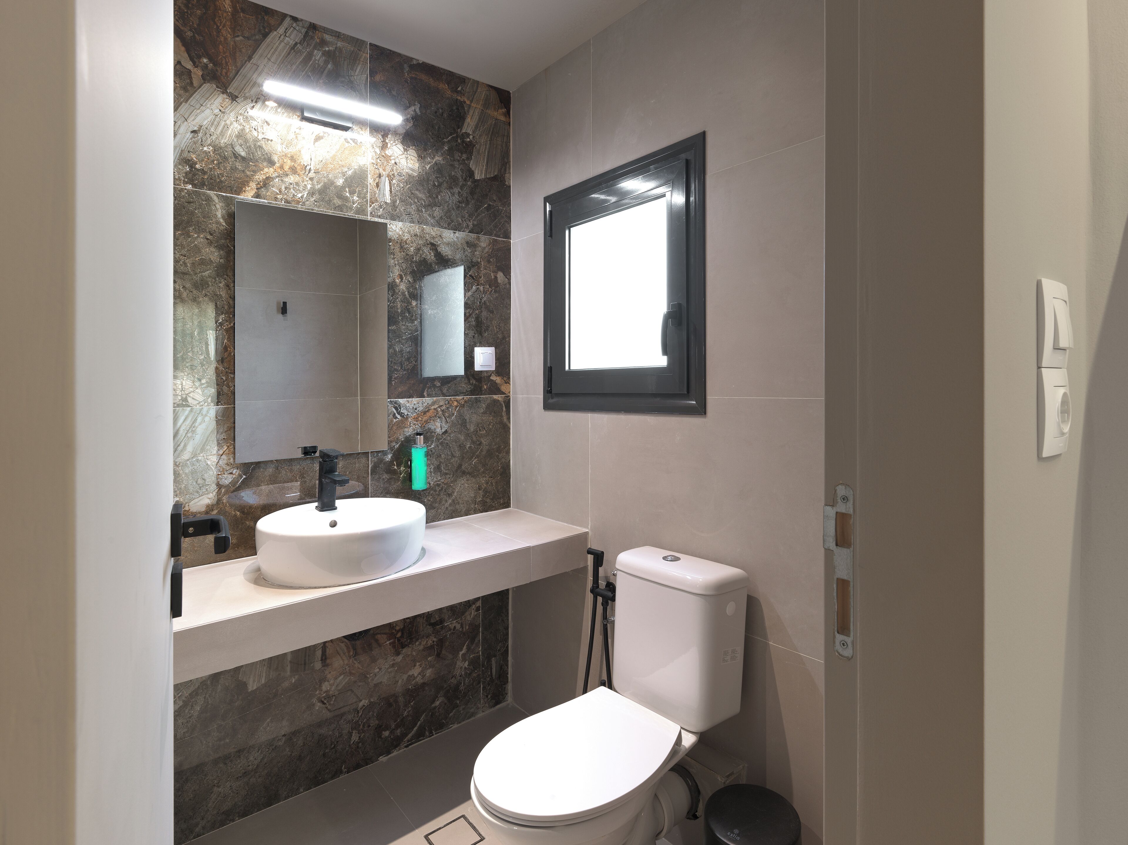 Un baño moderno con salpicadero de mármol, un lavabo blanco, un espejo y un inodoro.