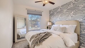 A bedroom with a bed, a ceiling fan, a window with blinds, a mirror, and a patterned wall.