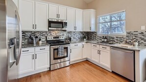 A modern kitchen with white cabinets, stainless steel appliances, a tiled backsplash, and a window providing natural light.