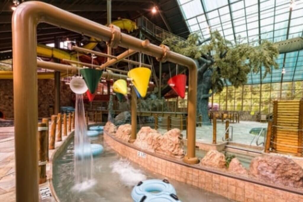 Ett inomhusområde med vattenlek, rutschkanor och en pool, omgivet av stenar och med ett glastak.