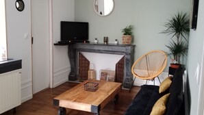A living room with a sofa, a coffee table, a fireplace, a television, and a mirror on the wall. - Pounette, apartment T2 RDC, 1 bedroom facing the thermal baths, villa des Tilleuls  (Luxeuil-les-Bains)