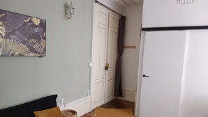 A room with a dark-colored sofa, a white door, a wooden floor, and a wall-mounted light fixture. - Pounette, apartment T2 RDC, 1 bedroom facing the thermal baths, villa des Tilleuls  (Luxeuil-les-Bains)