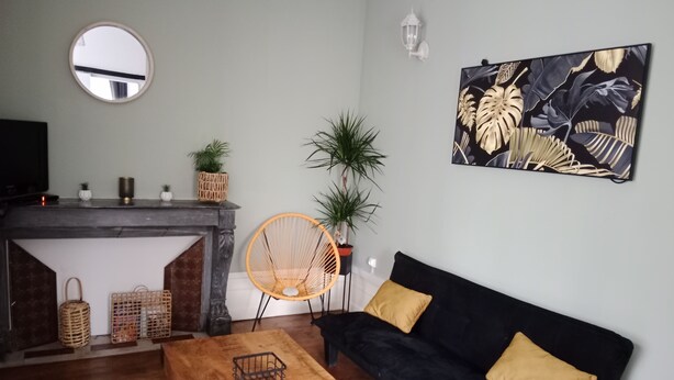 A living room with a fireplace, a black sofa with yellow cushions, a wooden coffee table, wicker baskets, and a large painting on the wall. - Pounette, apartment T2 RDC, 1 bedroom facing the thermal baths, villa des Tilleuls  (Luxeuil-les-Bains)