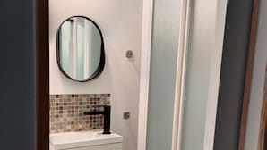 A bathroom with a white sink, a mirror, and a glass shower enclosure. - Pounette, apartment T2 RDC, 1 bedroom facing the thermal baths, villa des Tilleuls  (Luxeuil-les-Bains)