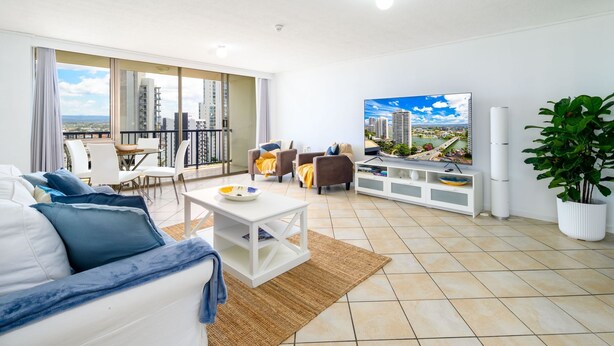 Un salón moderno con balcón, muebles blancos, un televisor de pantalla plana y vistas a la ciudad.