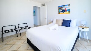 Una habitación de hotel con una cama grande, dos sillas metálicas negras, un cuadro de una furgoneta y una mesita de noche con una lámpara.