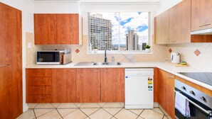 Una cocina moderna con armarios de madera, microondas integrado, lavavajillas y vistas a edificios de la ciudad a través de un ventanal.