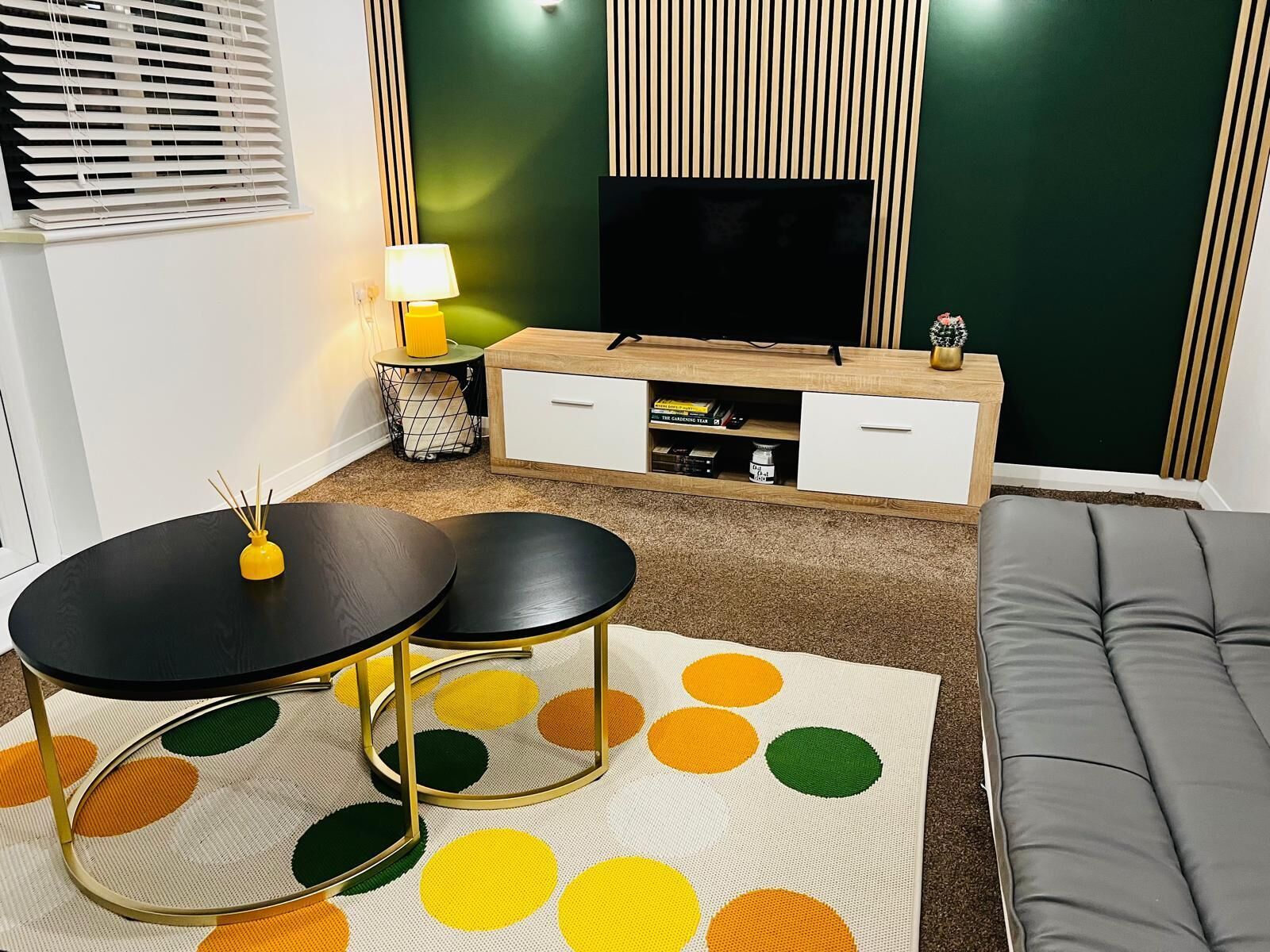 A modern living room with a black and white TV stand, a grey sofa, and a polka dot area rug.