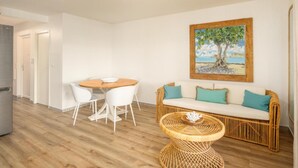 Een moderne woonkamer met een rieten bank, een ronde houten tafel en een schilderij van een boom.