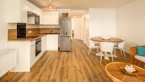 Een moderne keuken met witte kastjes, een roestvrijstalen koelkast en een houten aanrecht. Er is een eethoek met een ronde tafel en witte stoelen.