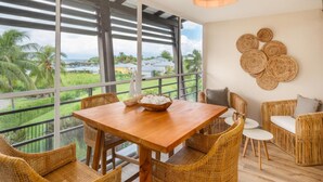 Een eethoek met een houten tafel en rieten stoelen, met uitzicht op een weelderig landschap met palmbomen en zee.