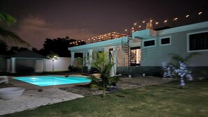 Propiedad residencial de noche con piscina, patio cubierto y escalera que lleva a un segundo piso.