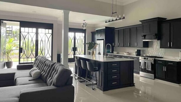 Cocina moderna con armarios oscuros, una isla central y un comedor con sofá y sillas.