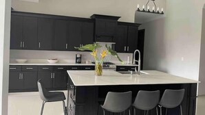 Una cocina moderna con armarios oscuros, una isla blanca y taburetes de bar.