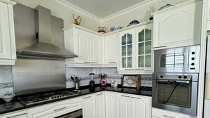 Eine Küche mit weißen Schränken, einem schwarz-weißen Schachbrettboden, einer Edelstahl-Dunstabzugshaube, einem Einbauofen und einem Kühlschrank.