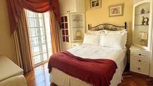 Ein Schlafzimmer mit Bett, Nachttisch, Stuhl, Deckenventilator und einem Fenster mit Vorhängen.