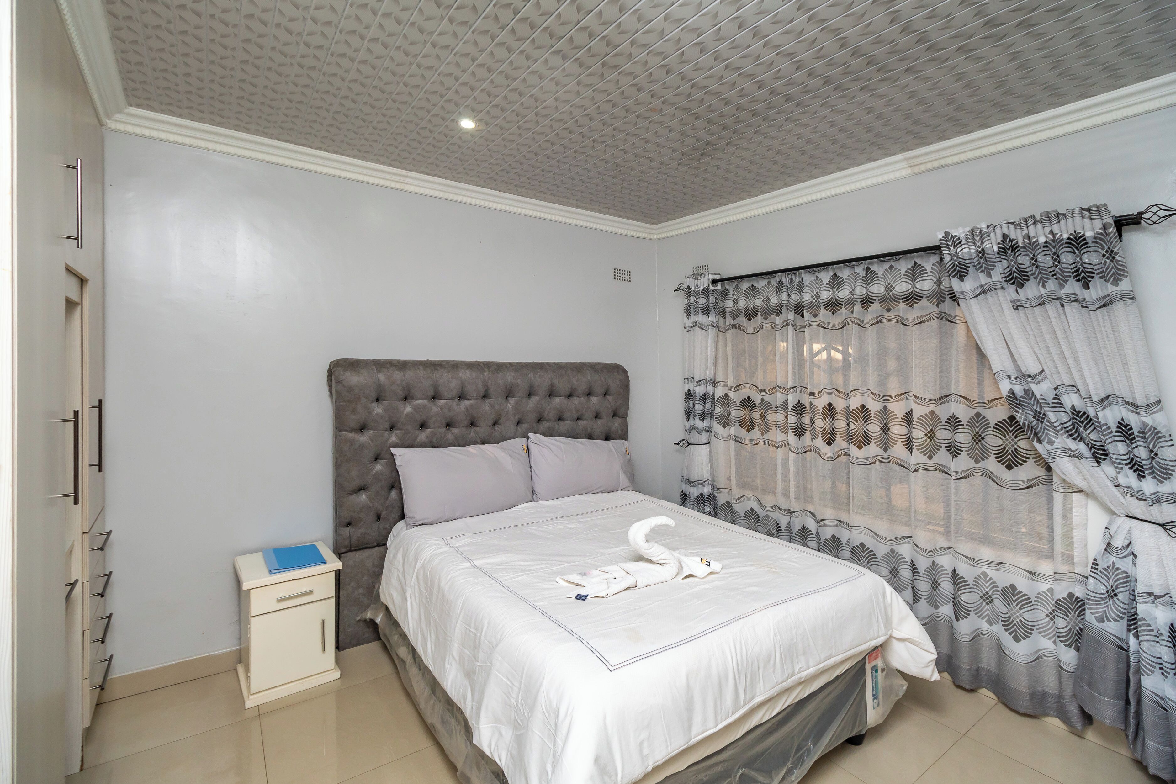 Un dormitorio con cabecera capitonada, cama bien hecha, mesita de noche con un libro y ventana con cortinas estampadas.