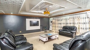 Ein Wohnzimmer mit schwarzen Ledersofas, einem Couchtisch, einem an der Wand montierten Fernseher und einer Kristallleuchtre.
