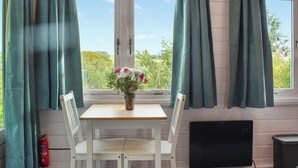 Een kamer met een tafel en twee stoelen, een vaas met bloemen, een brandblusser en een raam met gordijnen.
