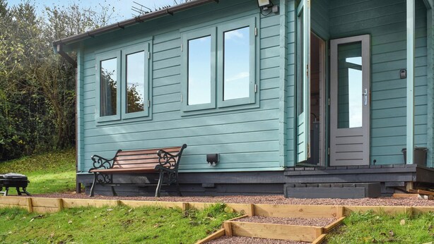 Een lichtblauwe houten woning met een bankje, een deur en een kleine tuin met verhoogde bakken.