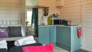 Een compacte kamer met een kitchenette, een bed met kussens en een klein tafeltje met een stoel.
