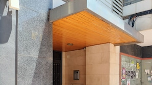 Entrada de un edificio con suelo de baldosas, techo de madera y puerta con cerradura electrónica.
