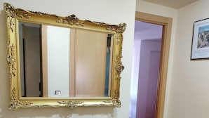 Una habitación con un espejo grande y ornamentado, un mueble de madera con cajones, una encimera de mármol y una vela roja sobre un plato de vidrio.