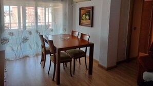 Un comedor con una mesa y sillas de madera, un cuadro en la pared y una ventana con cortinas traslúcidas.