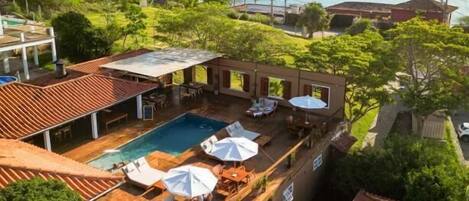 A rooftop pool area with lounge chairs and umbrellas, surrounded by lush greenery and overlooking a scenic bay.