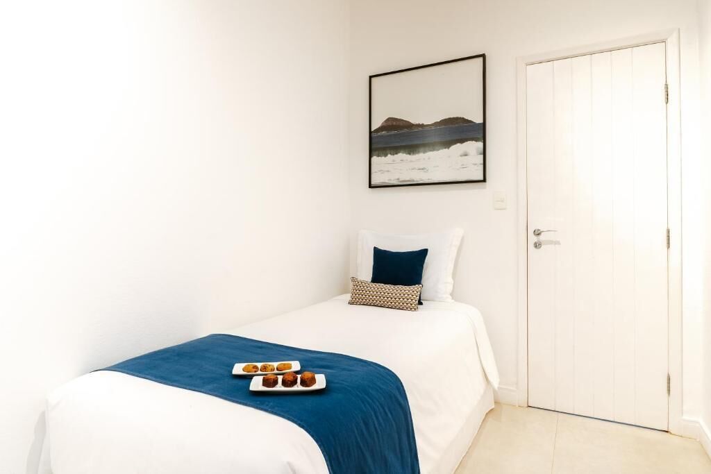 A bedroom with a bed, a bedside table, a nightstand, a framed picture on the wall, and a door.